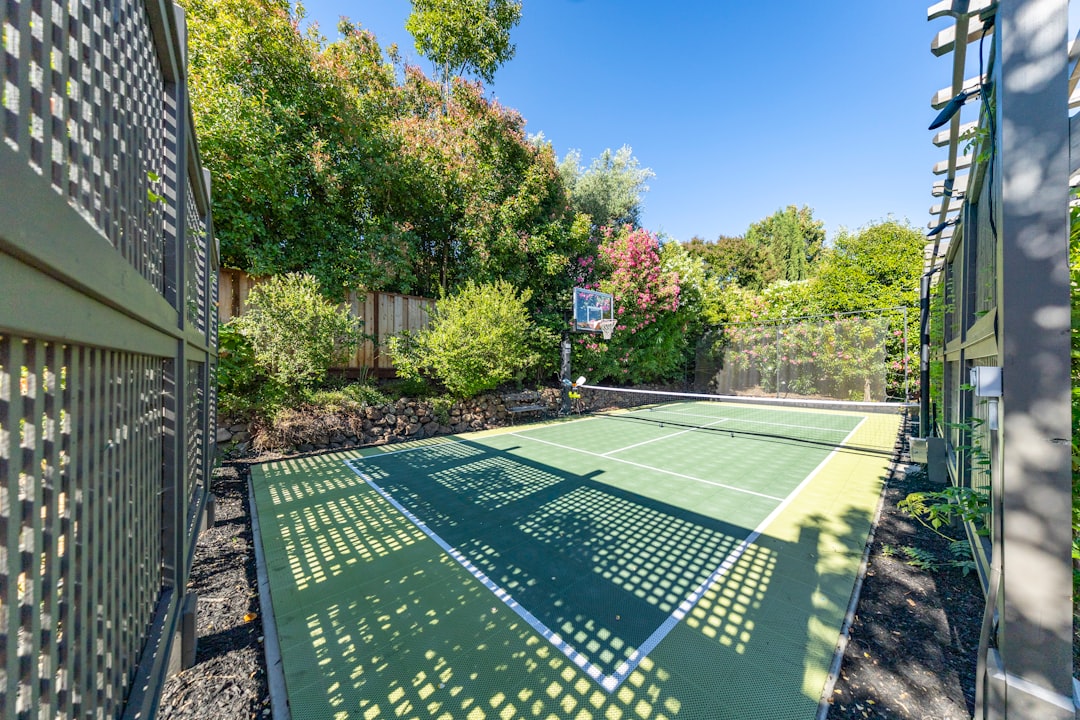 Outdoor pickleball court with basketball hoop surrounded by lush greenery. vintage pickleball court, wooden paddles, outdoor backyard game, 1960s family