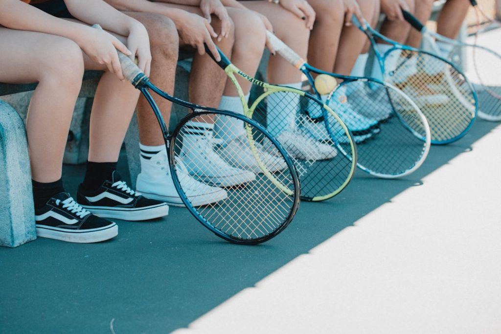 person in black and white nike sneakers holding blue and white tennis racket tennis rackets lineup on court, beginner tennis equipment, tennis balls and rackets