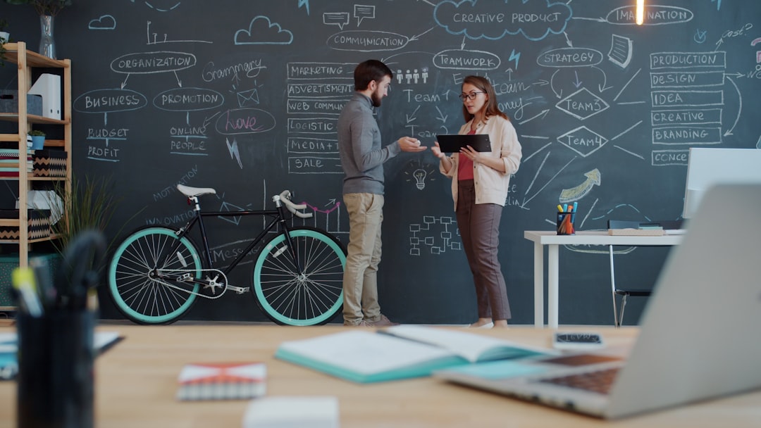 Two people discuss a plan on a chalkboard wall. team collaboration software dashboard, knowledge base interface, modern office workspace