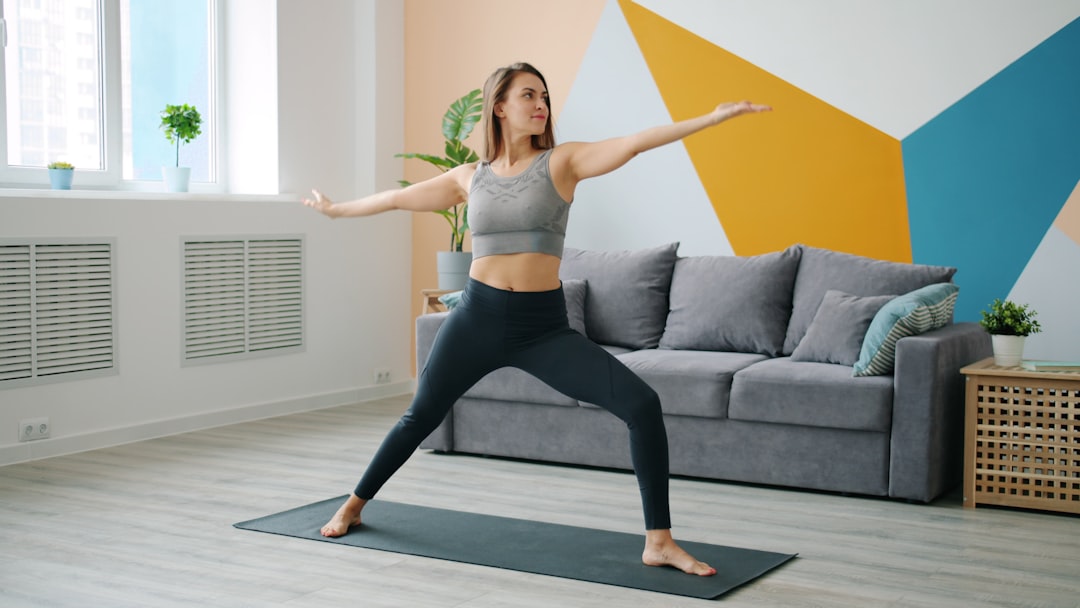 Woman practicing warrior ii pose on yoga mat. woman doing mat pilates at home, yoga mat, bright living room workout