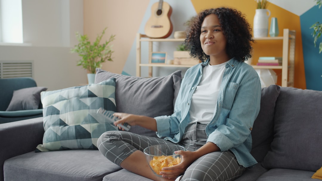 Young woman watching TV and eating snacks on couch. cricket streaming laptop snacks living room